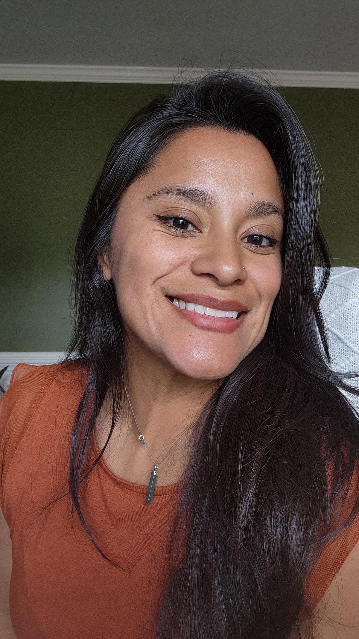 Yessie Perez smiling at home, in an orange top in front of a green wall